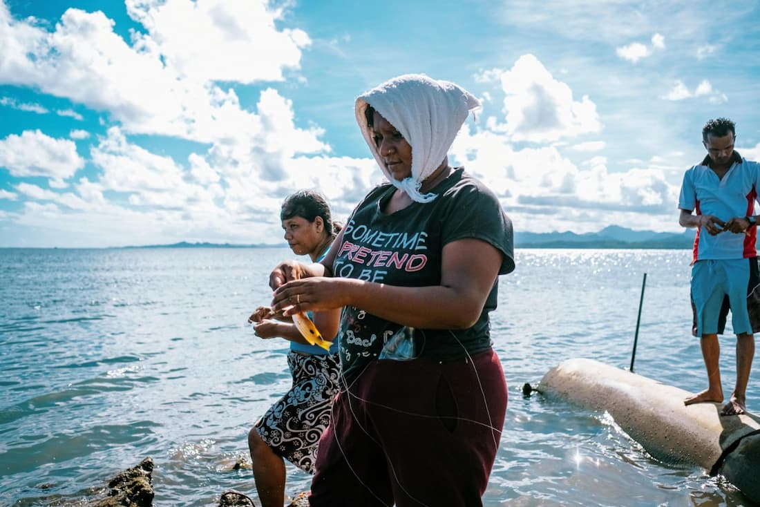 A family fishing for small fish in Suva harbor, standing on the storm drains that extend out into the water.