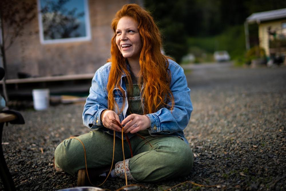 Marina Anderson, Program Director of the Sustainable Southeast Partnership, smiles while sitting on the ground and weaving cedar.