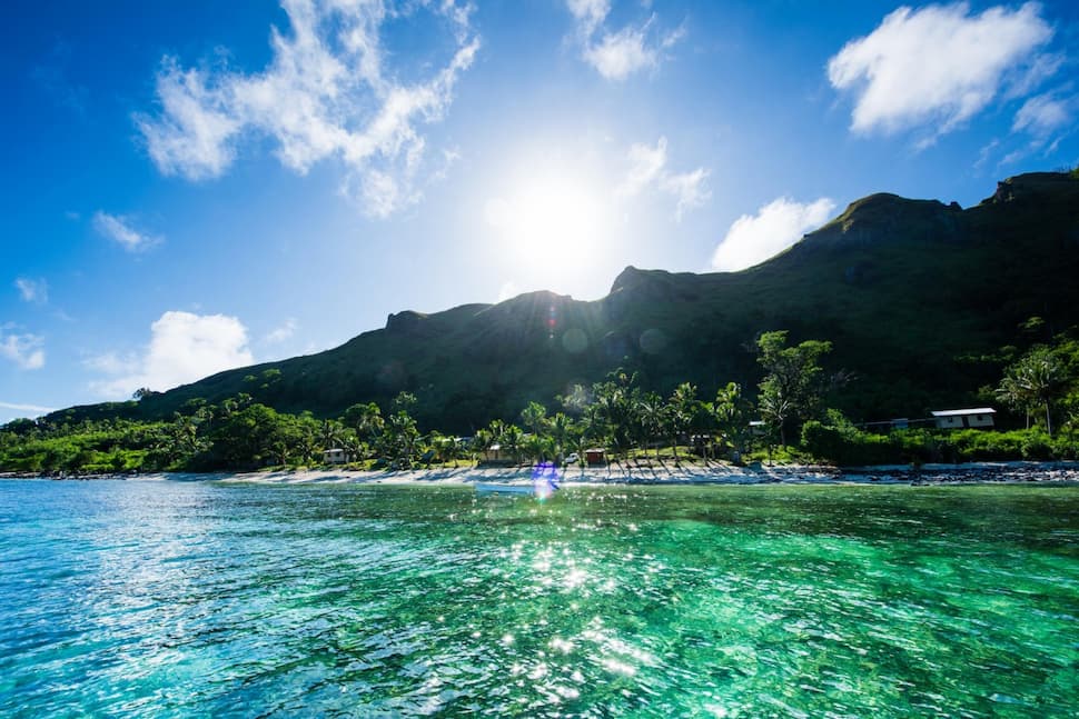 Beautiful Kia Island off the northern coast of Vanua Levu with clear blue ocean waters, beach, trees and mountains in the distance.